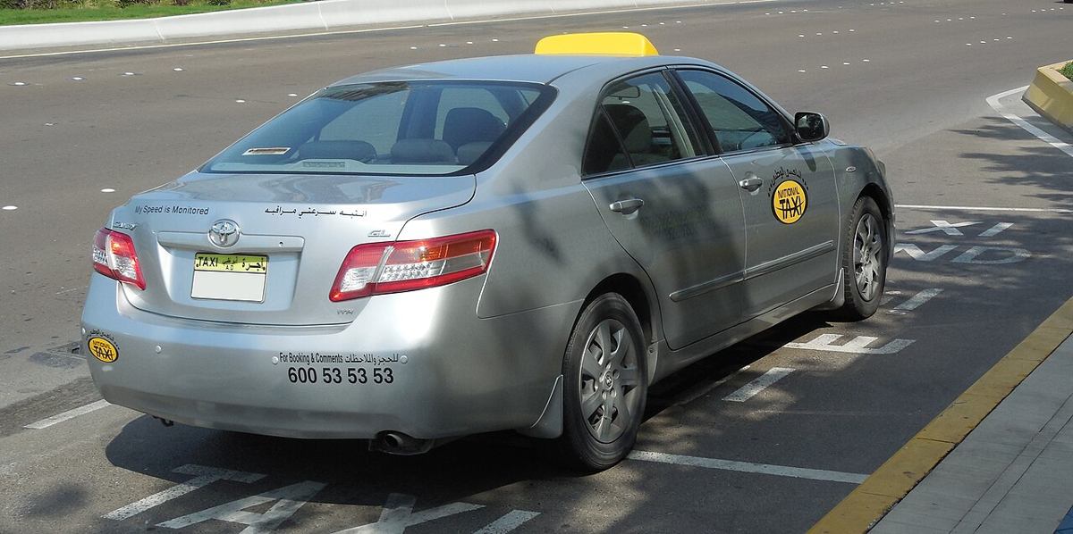 Licensed silver taxi with yellow roof light on an Abu Dhabi road
