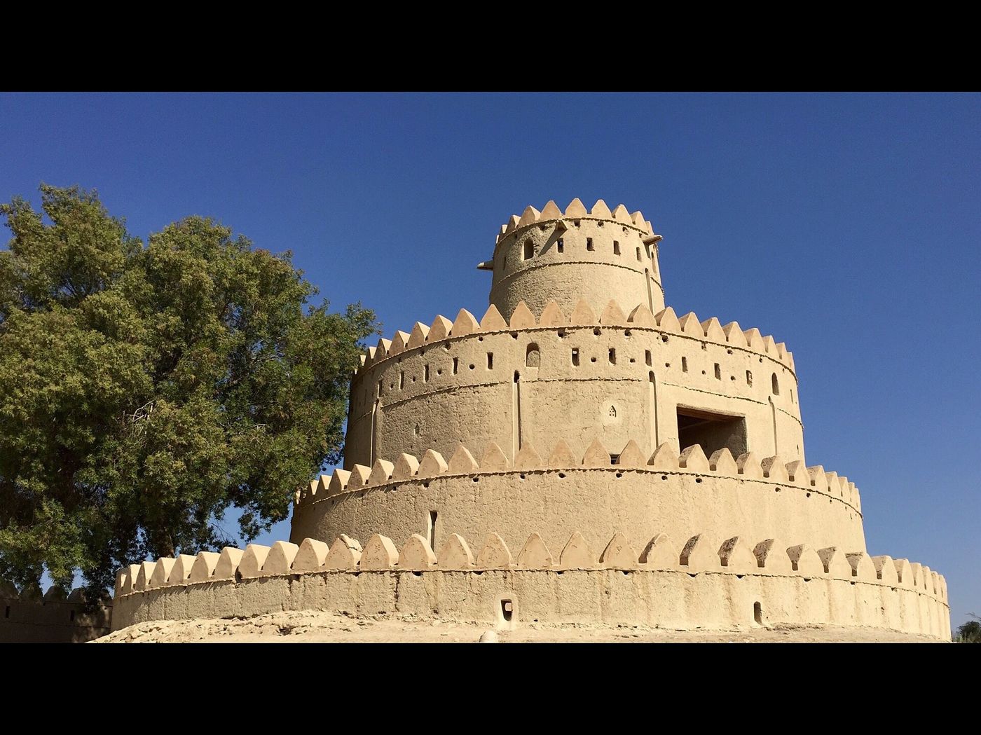 Sunlit exterior wall and round tower of Al Jahili Fort in Al Ain